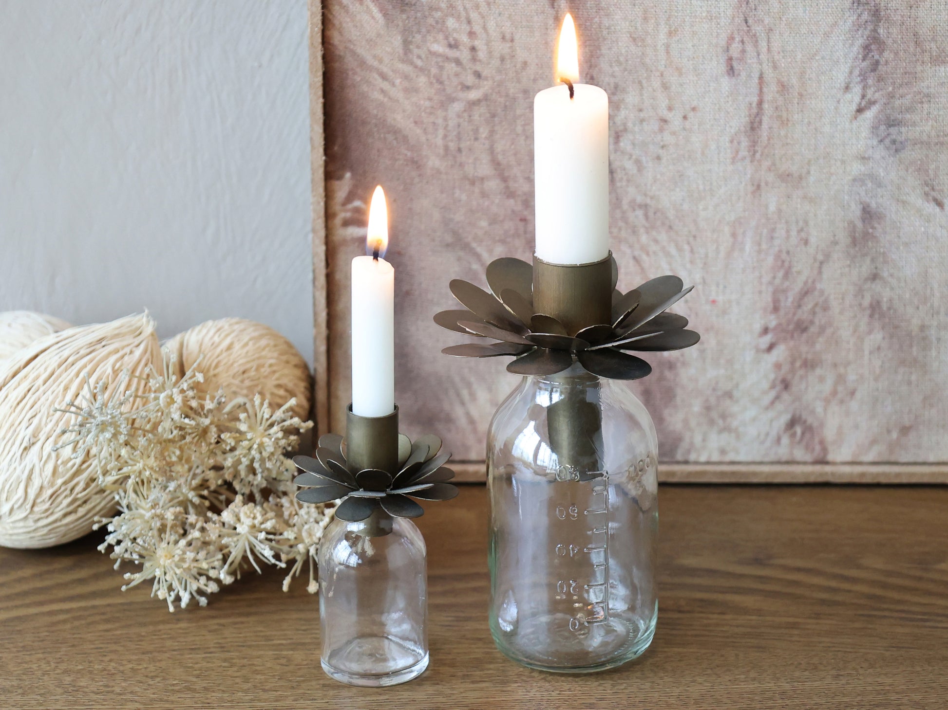 Two glass bottles with metal candle holders holding candles on a wooden surface.