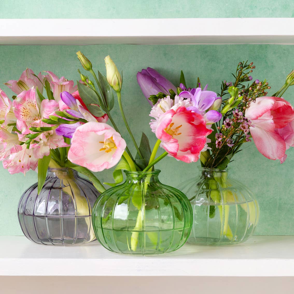 Green, lilac and clear bud vases with flowers on table top