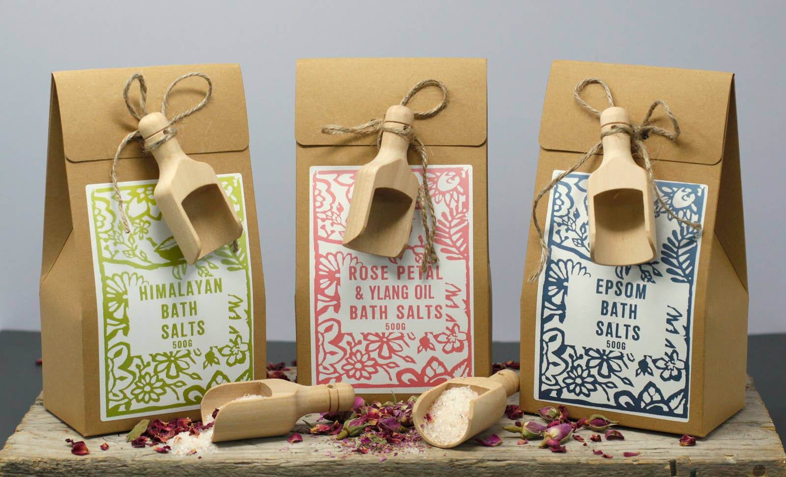 Assortment of Agnes + Cat Bath Salts sitting on a table with wooden scoop and rose petals