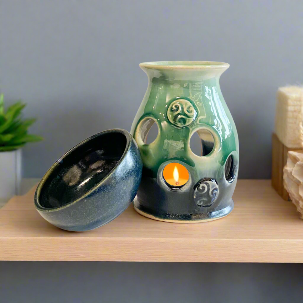 Pretty hand thrown stoneware wax burner in blue and green glaze with Celtic design accents sitting on a shelf