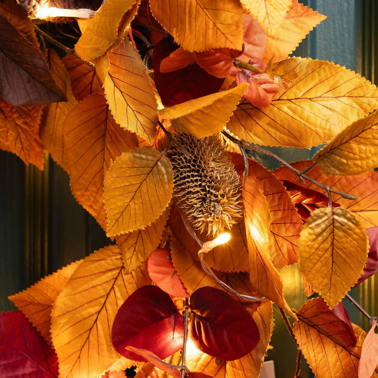 Close-up of an autumn-themed artificial leaf garland with glowing fairy lights, featuring golden yellow, orange, and deep red leaves.