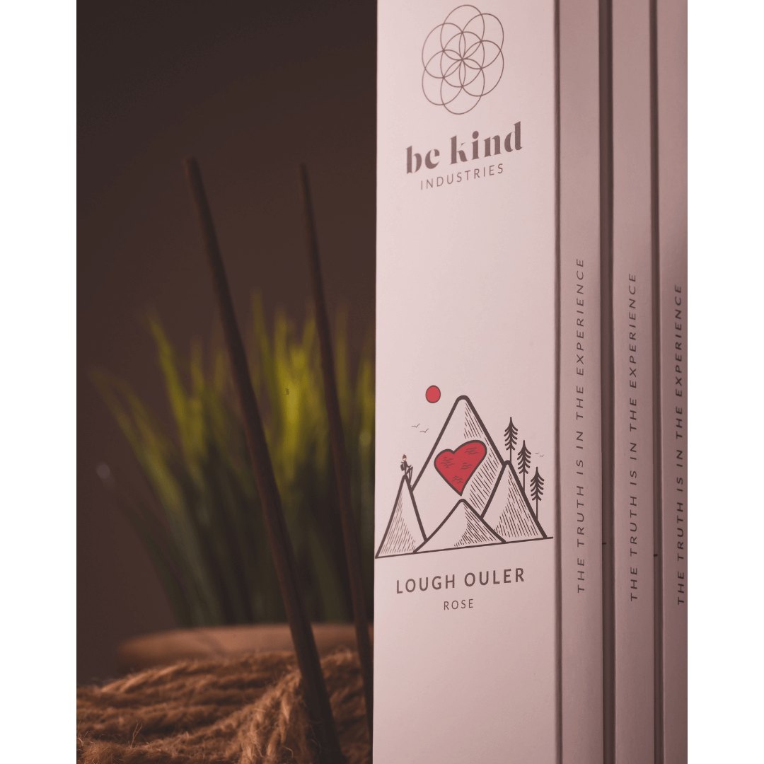 Packages of Be Kind brand incense sticks, labeled 'Lough Ouler- Rose' with a minimalist design standing upright with plants in the background