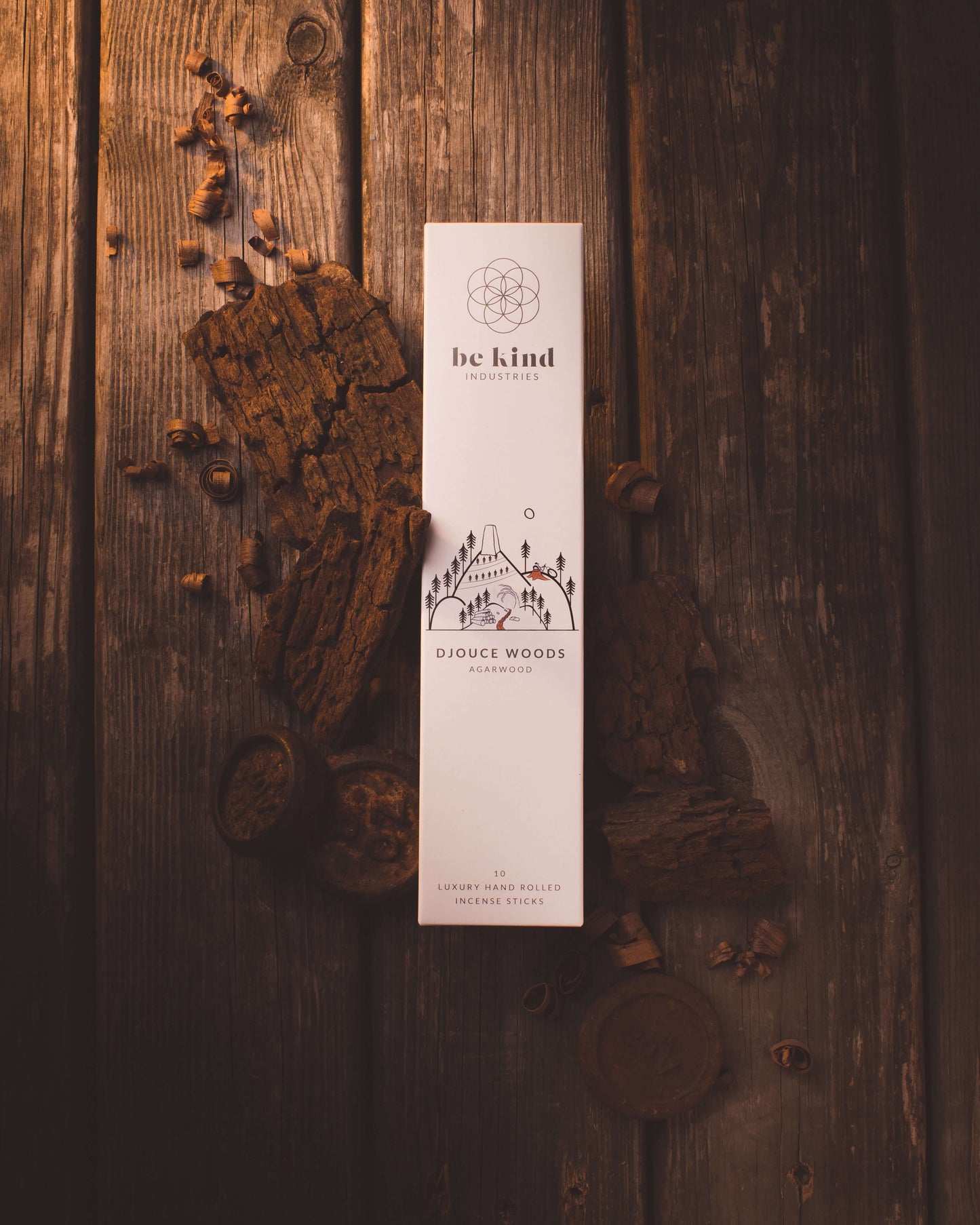 A package of Be Kind brand incense sticks, labeled 'TDjouce woods' with a minimalist design on a rustic table