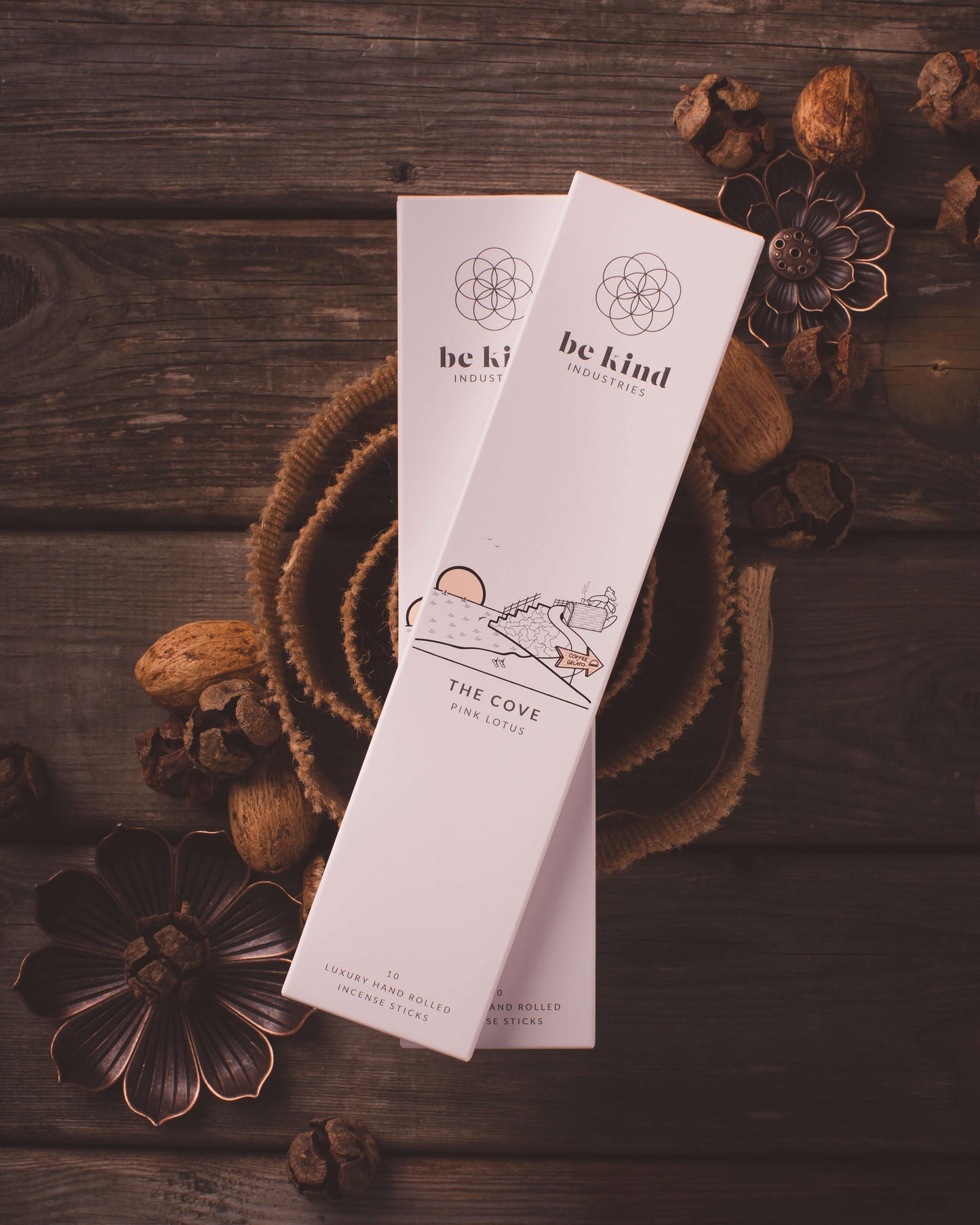 A package of Be Kind brand incense sticks, labeled 'The Cove - Pink Lotus' with a minimalist design sitting on a rustic table