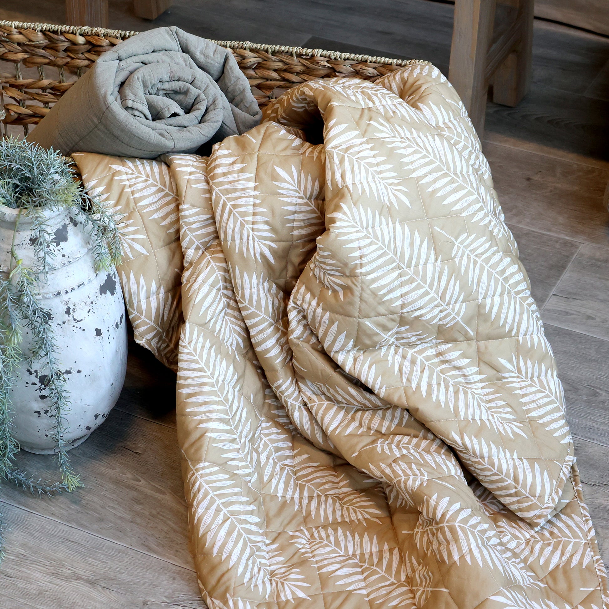 beige white tropical leaf quilt draped over a basket in a stylish interior setting.