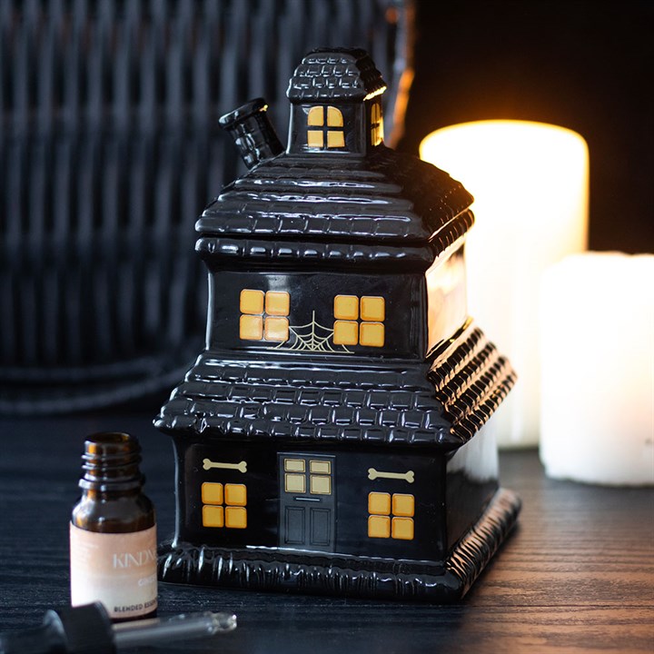 Black haunted house-shaped wax warmer with glowing windows on a dark surface.