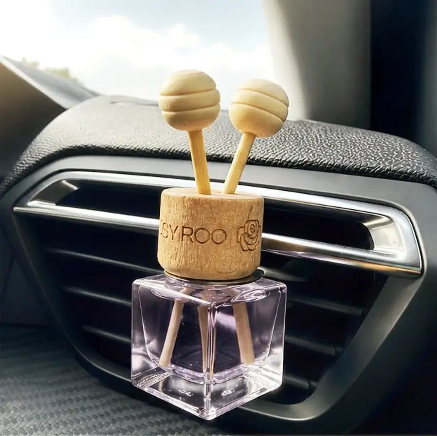 A car air freshener with a clear square bottle and a natural wood top featuring two wooden diffuser sticks with honeycomb-patterned ends. The top is engraved with the brand name 'SYROO'.