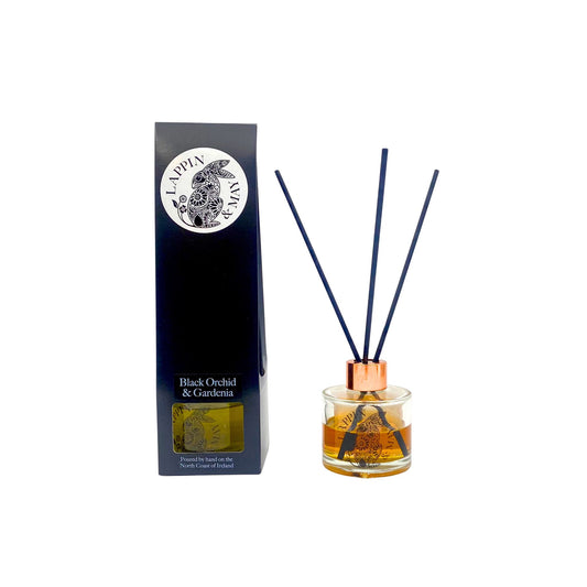 A Black Orchid & Gardenia Reed Diffuser set on a white background, consisting of a glass bottle with liquid and a copper cap, alongside three blue reeds and a black packaging box with a floral design.