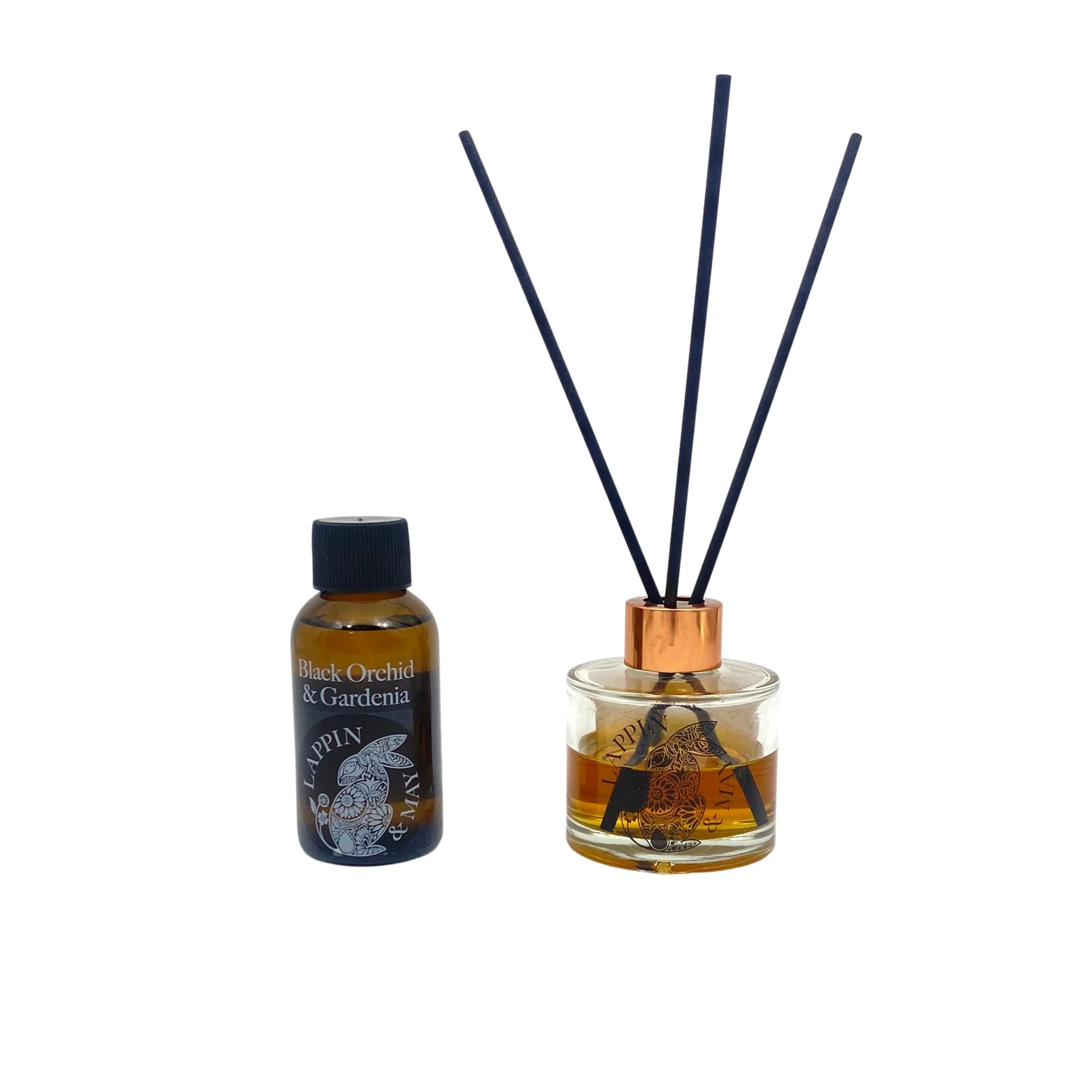 A bottle of Black Orchid & Gardenia refill with a black label and a copper-colored cap, next to a diffuser with a visible clear bottle and a black label.