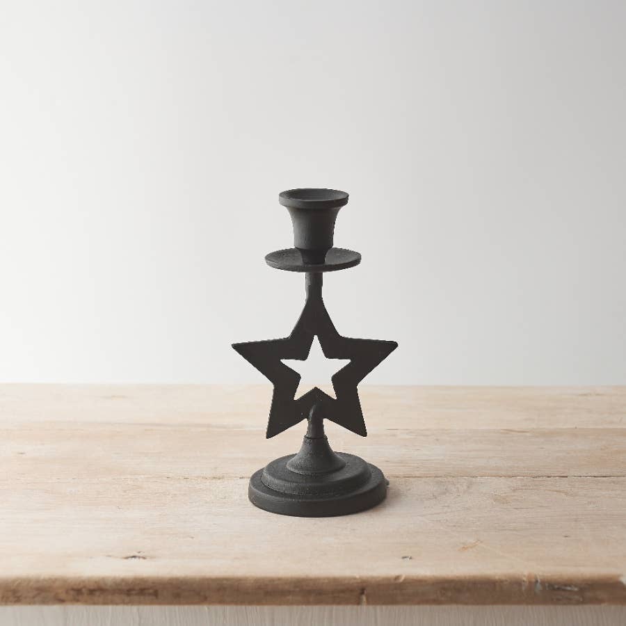 Black star-shaped candle holder on a wooden surface with a white background