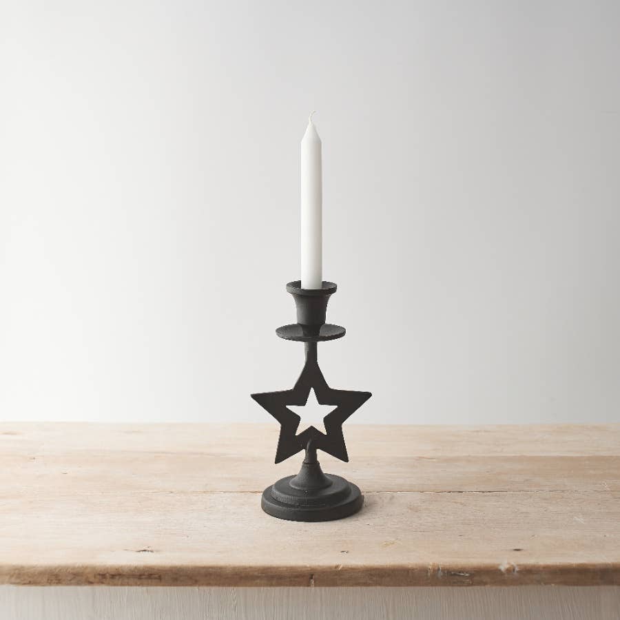 Black star-shaped candle holder with a white candle on a wooden surface