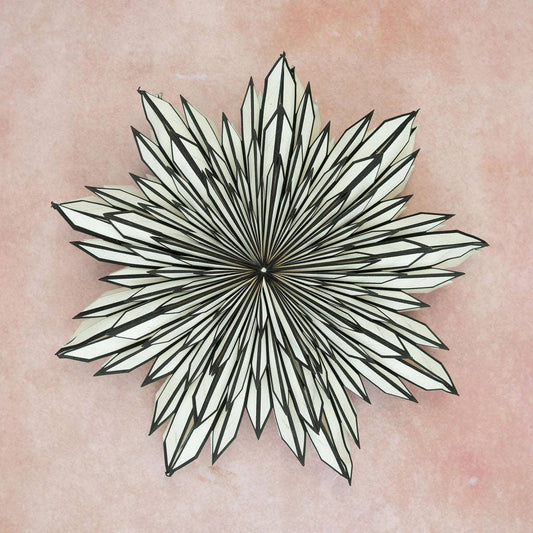 A black and white paper wall decoration designed in a floral pattern, displayed against a pink background.