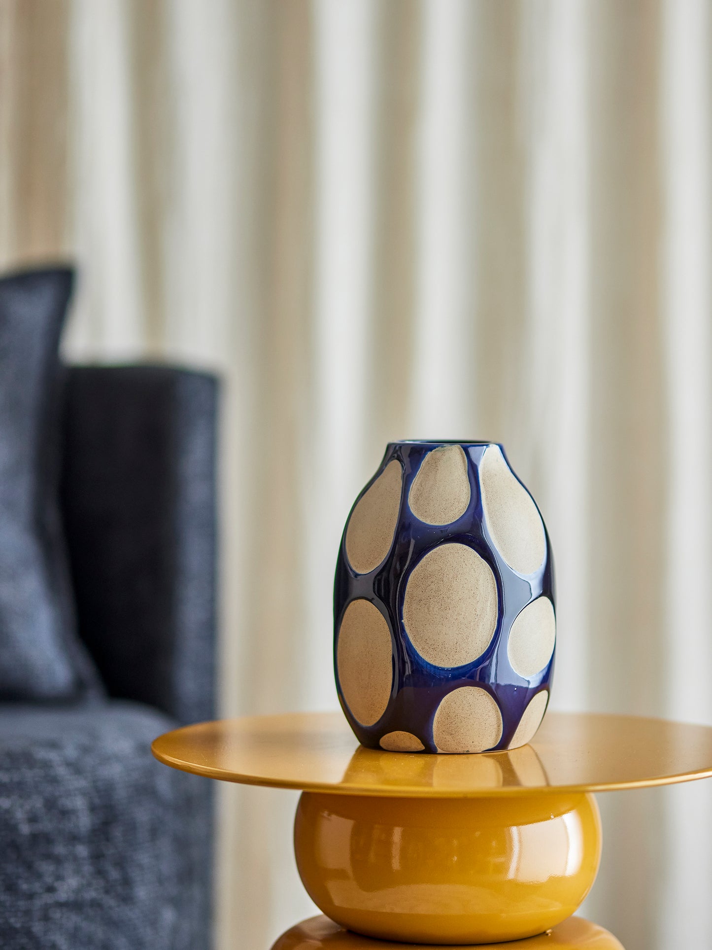 Decorative vase with blue and beige pattern on a yellow table against a neutral background