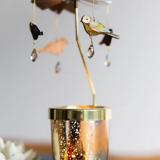 Decorative candle with bird and crystal mobile against a blurred background