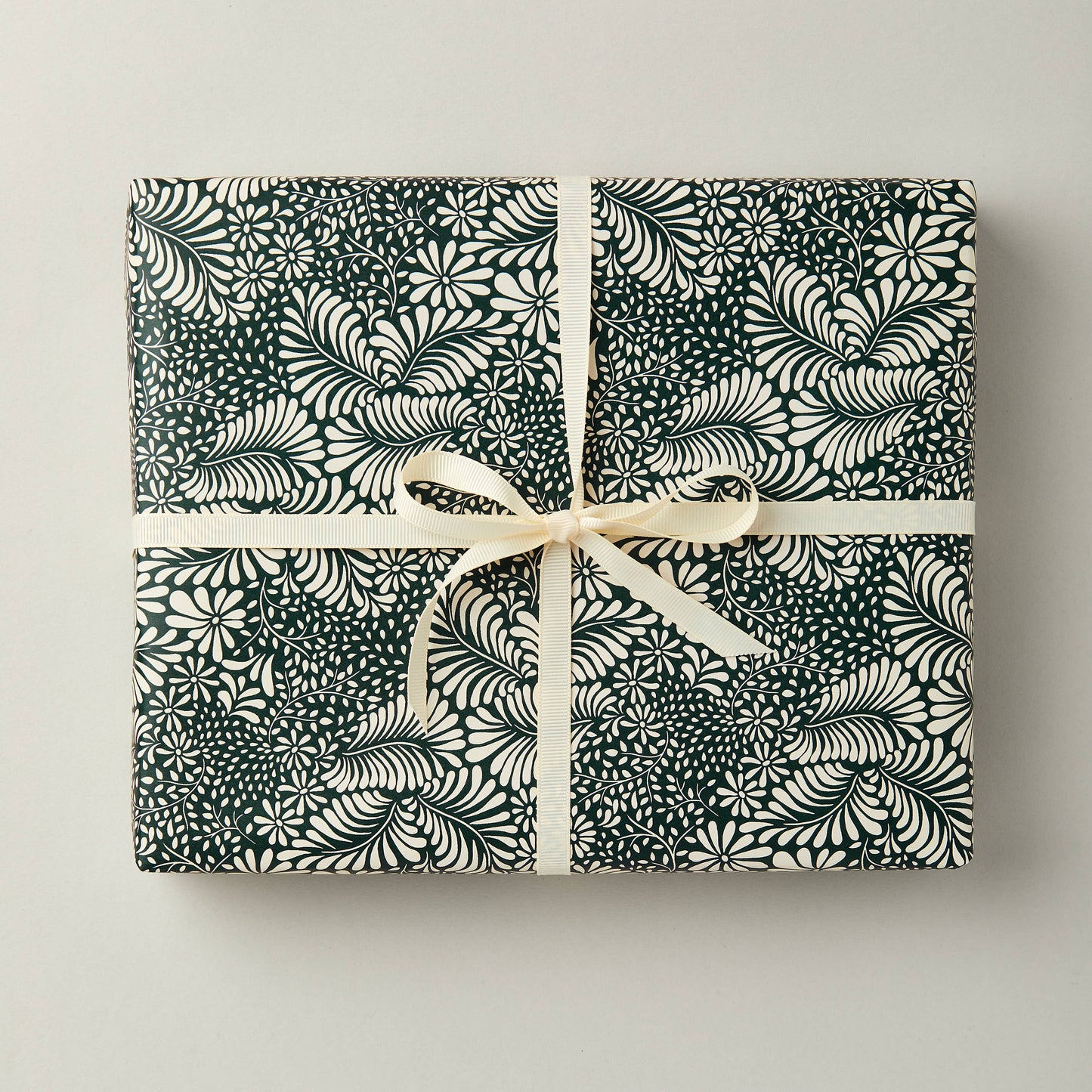 A sheet of green botanical gift wrap with a floral pattern, tied with a white ribbon.