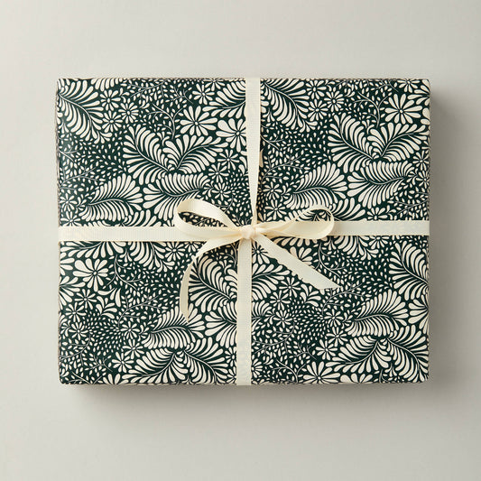 A sheet of green botanical gift wrap with a floral pattern, tied with a white ribbon.