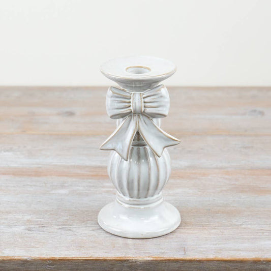 White ceramic candle holder with bow design on a wooden surface
