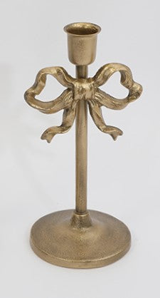 A vintage-style brass candlestick holder with a decorative bow motif on the stem, set against a plain light gray background.