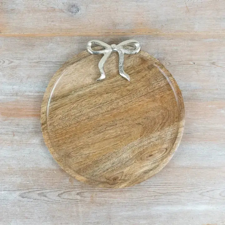 A round wooden serving board with a silver metal bow handle, photographed from directly above on a light wood plank surface.