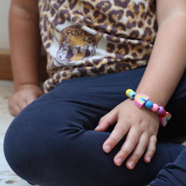 Person wearing a colorful bracelet sitting cross-legged on a wooden floor.