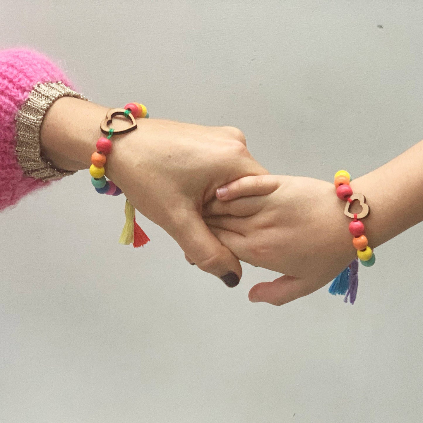 Two hands holding each other wearing colorful bracelets with heart charms on a plain background