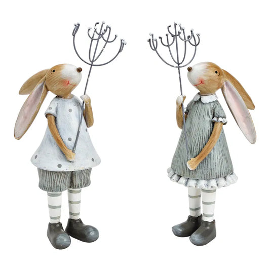 Two decorative rabbit figurines in dresses holding garden tools on a white background