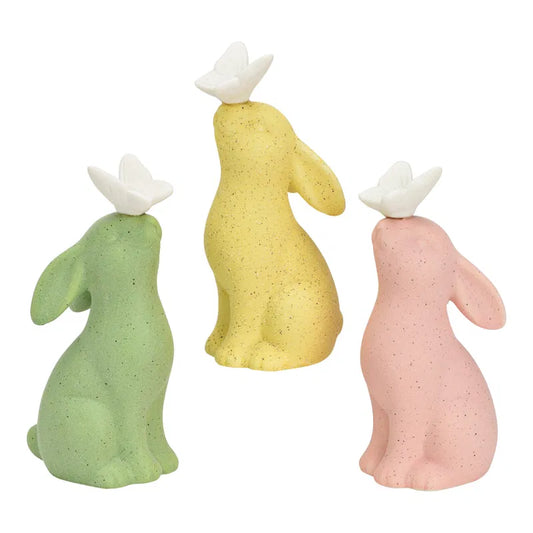 Three resin rabbit figurines in green, yellow, and pink on a white background