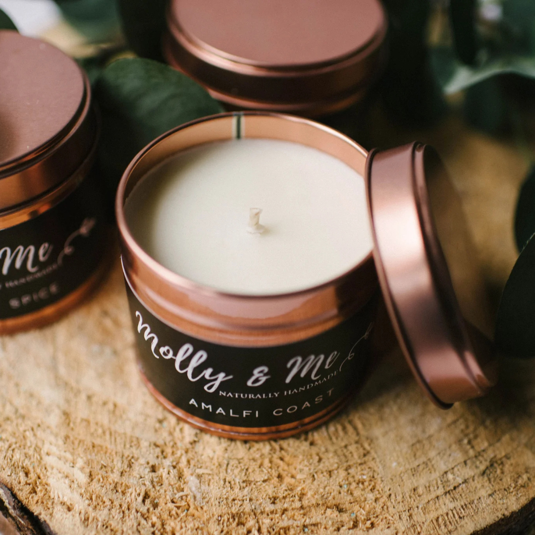 Candle in a copper tin with 'molly & me' branding on a wooden surface.