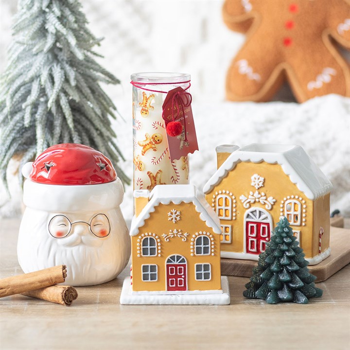 Decorative gingerbread house, Santa mug, and Christmas tree on a wooden surface with a blurred background.