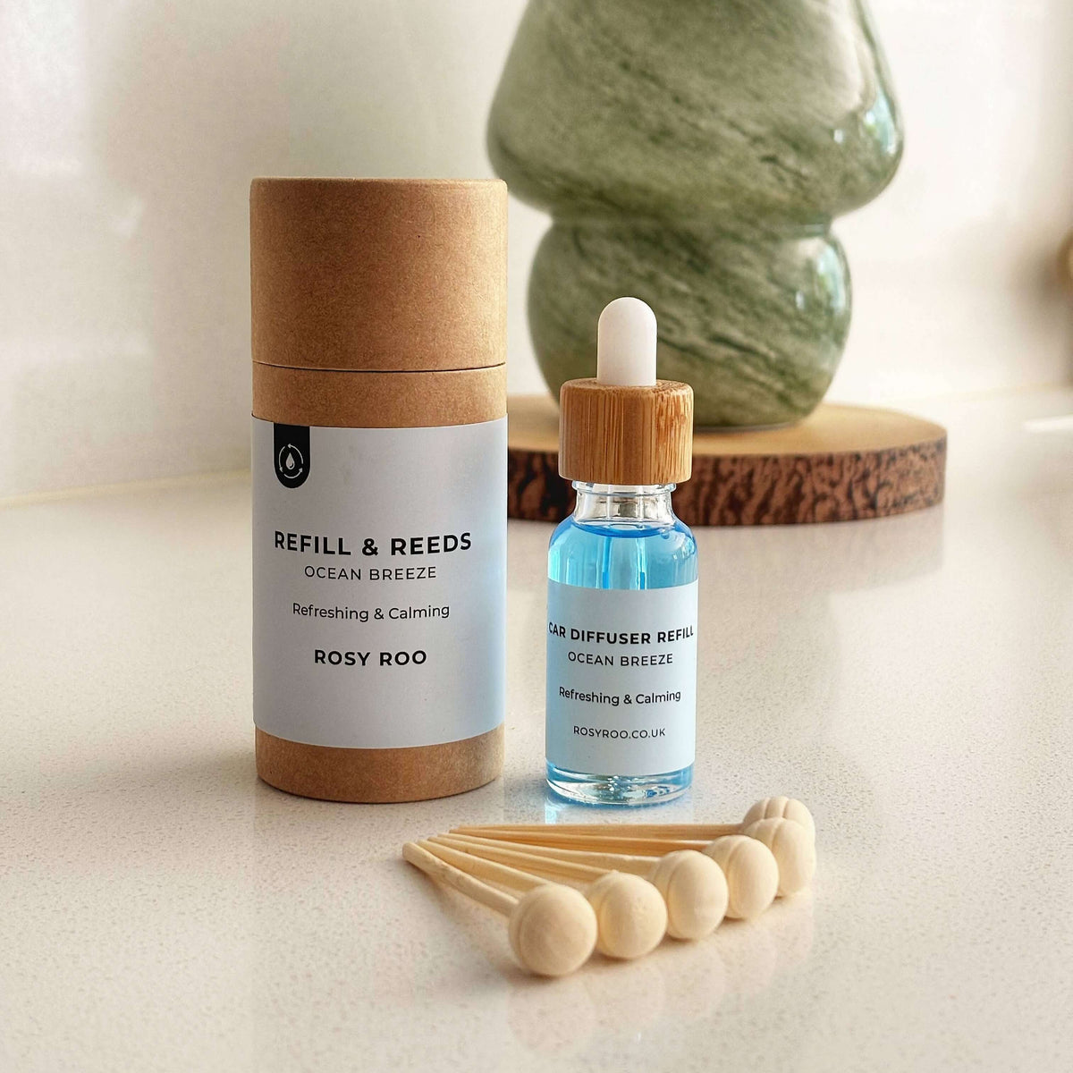 Diffuser oil bottle with wooden cap, cardboard sleeve, and wooden sticks on a light surface.