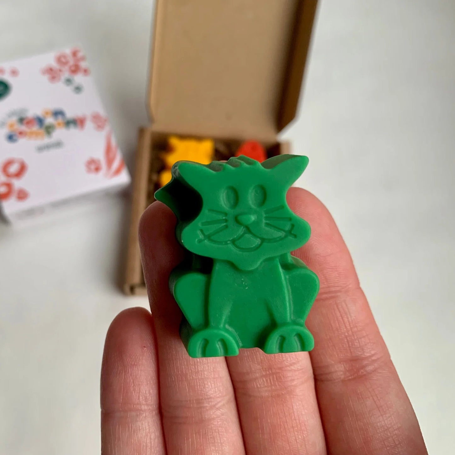 Green cat-shaped crayon held in a hand with a blurred background