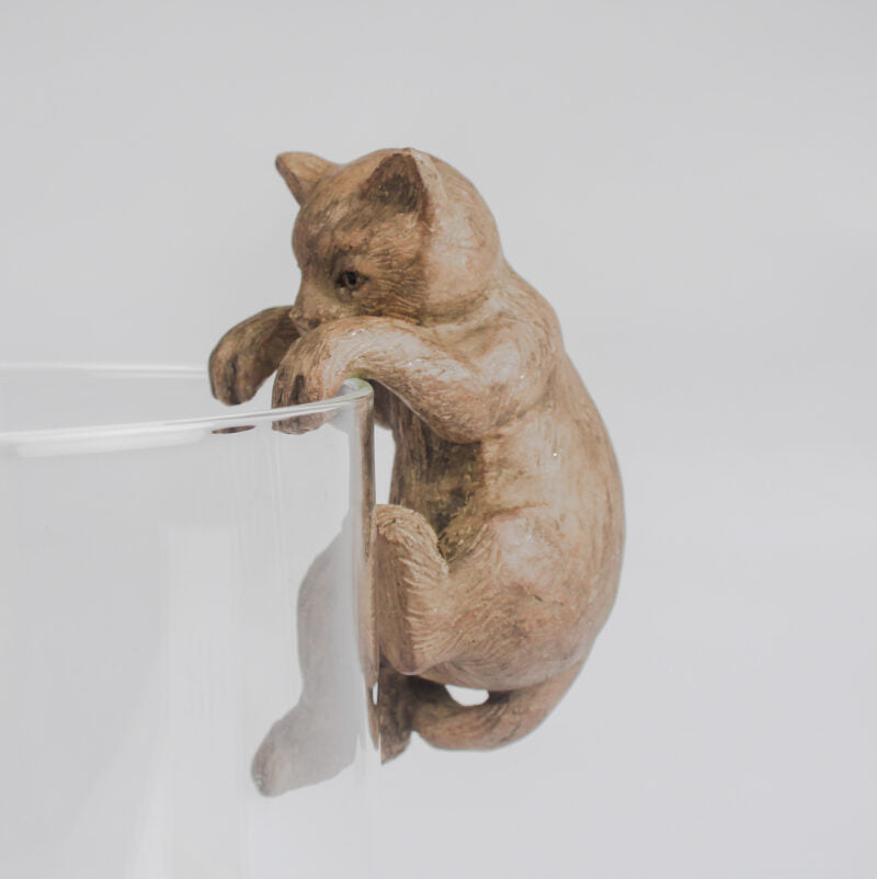 Resin cat figurine leaning against a clear glass on a light gray background