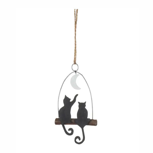 A hanging decorative ornament featuring two black cat silhouettes sitting on a wooden branch under a crescent moon, suspended by a rope against a plain white background.