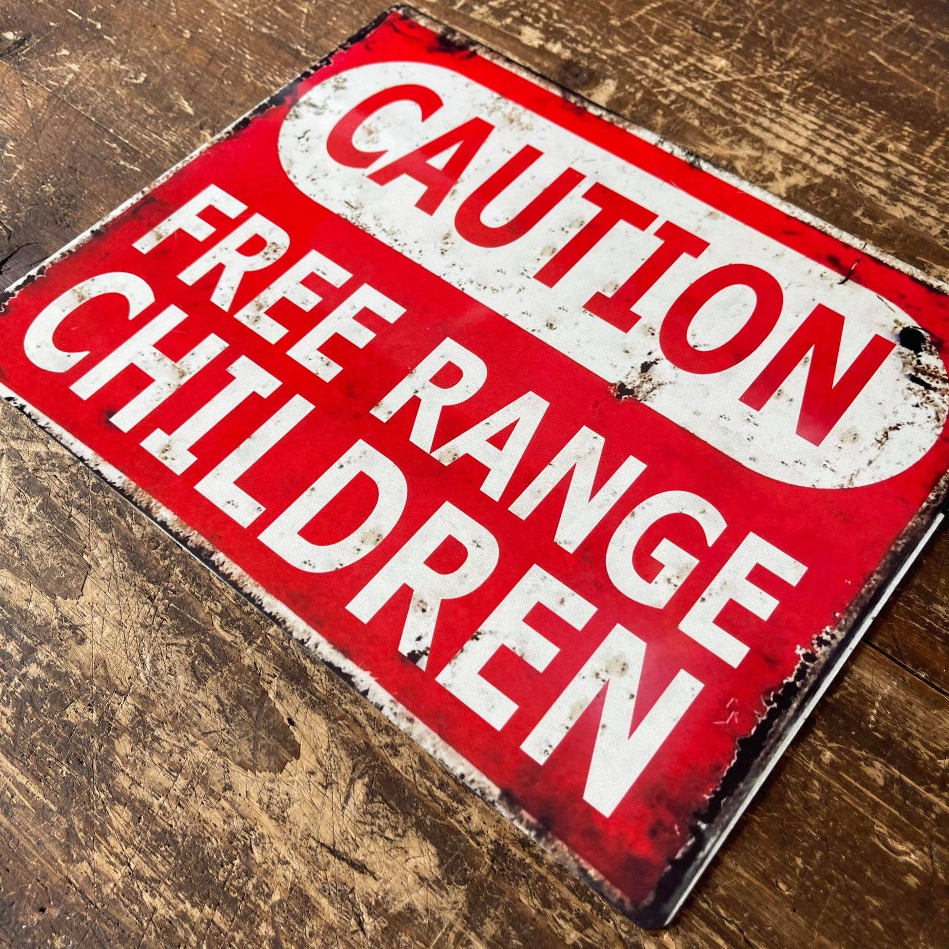 Vintage-style metal sign with 'Caution Free Range Children' text on a wooden surface