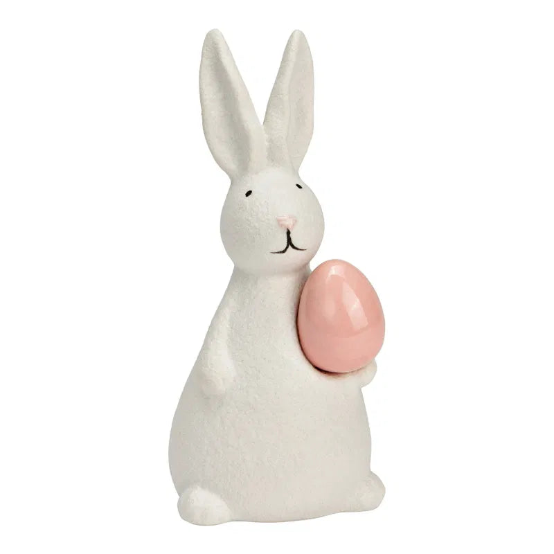 White ceramic bunny holding a pink egg on a white background