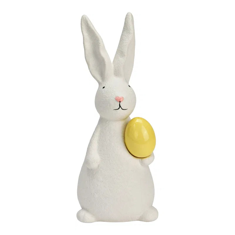 White ceramic bunny holding a yellow egg on a white background