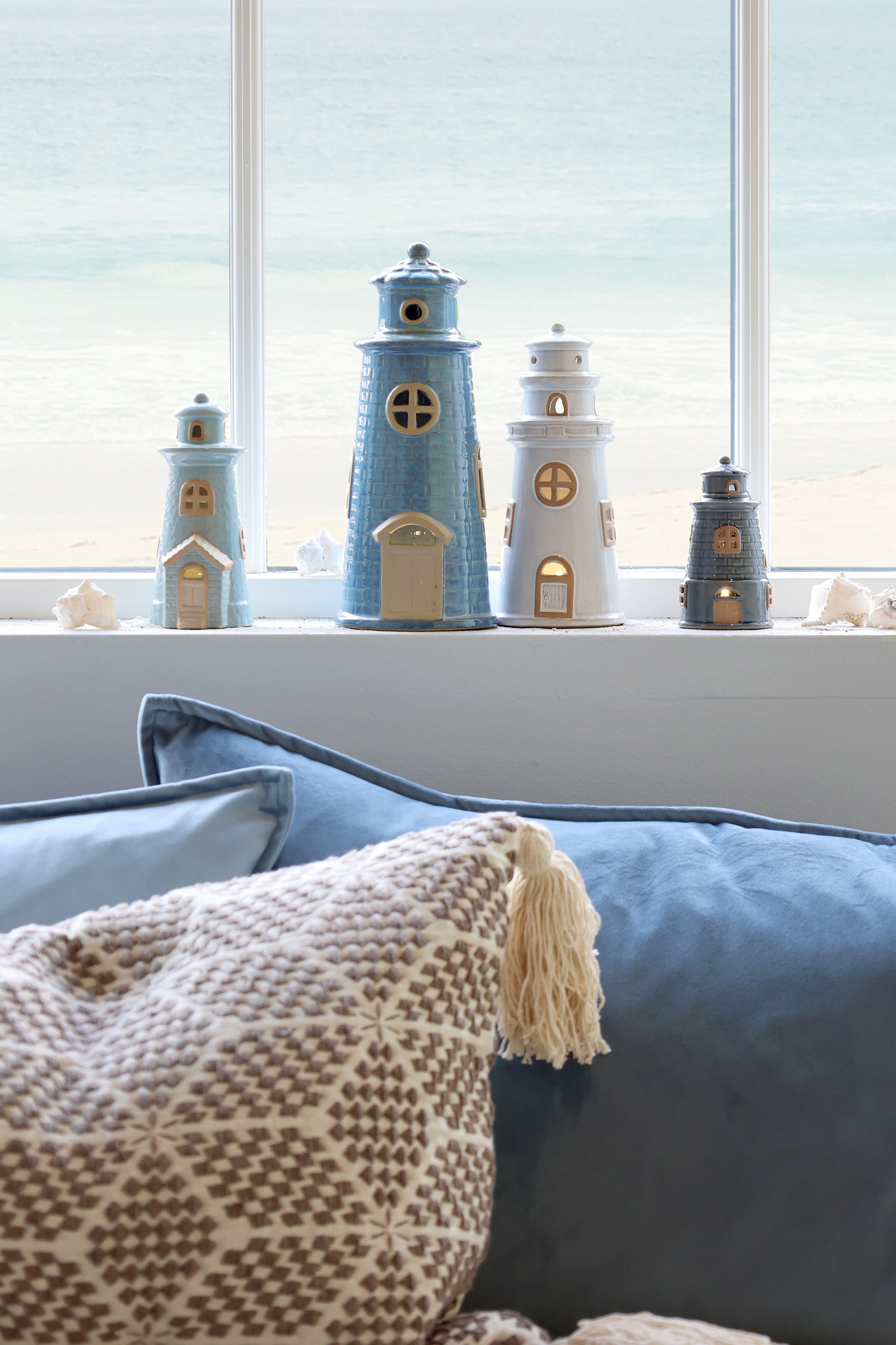 Decorative lighthouse models on a windowsill with a view of water.