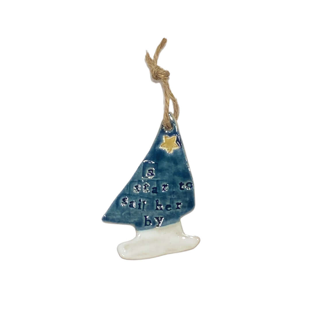 A ceramic hanging decoration in the shape of a yacht with blue and white colors and a yellow star, on a jute string.