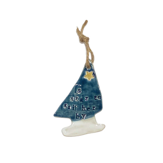A ceramic hanging decoration in the shape of a yacht with blue and white colors and a yellow star, on a jute string.