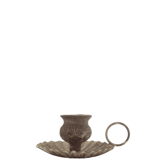 A small metallic candle holder with an embossed floral pattern, resting on a matching leaf-shaped saucer with a ring handle, shown against a plain white background.