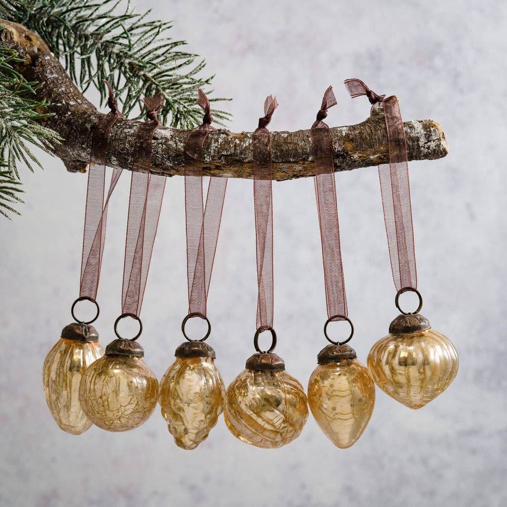Decorative gold glass ornaments hanging from a branch against a neutral background