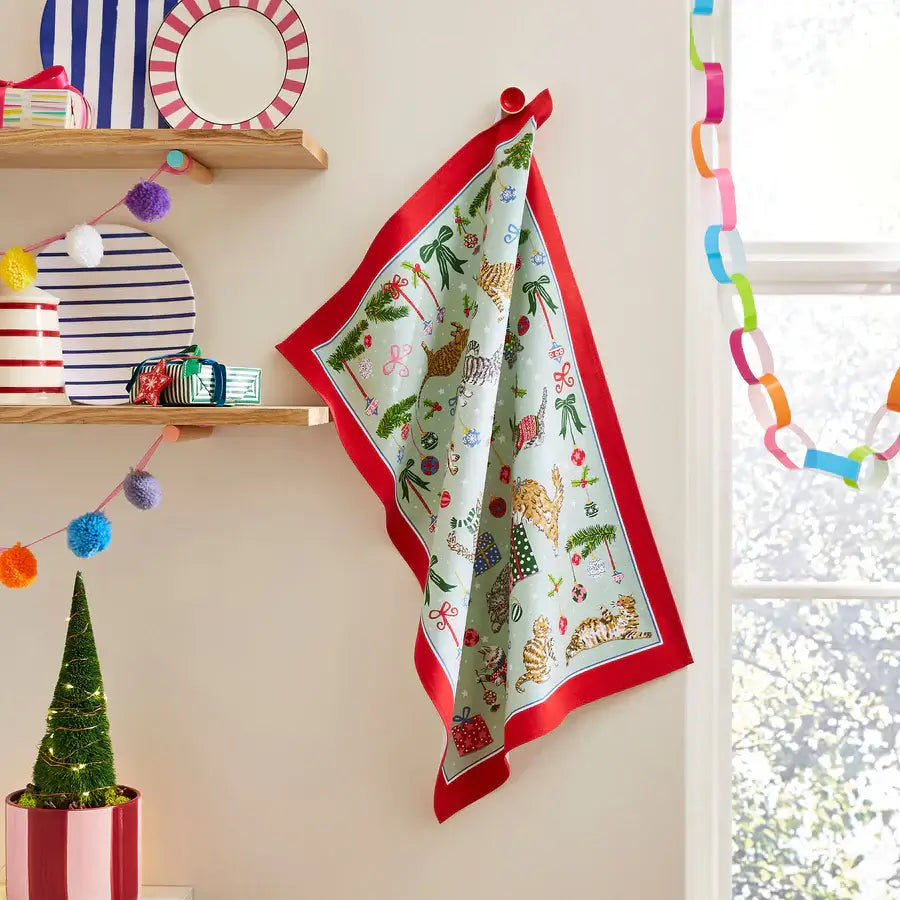 Decorative towel with festive design hanging on a wall next to a window with colorful decorations.