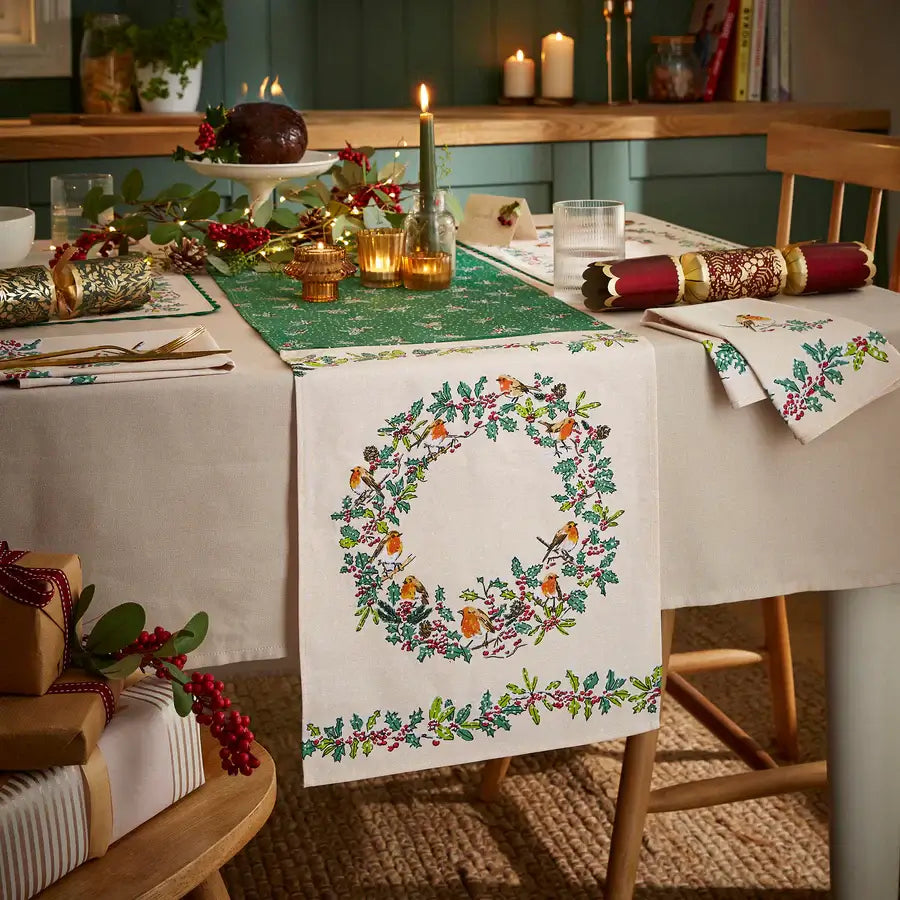 Decorative table setting with a embroidered tablecloth featuring a wreath design, candles, and Christmas decorations.