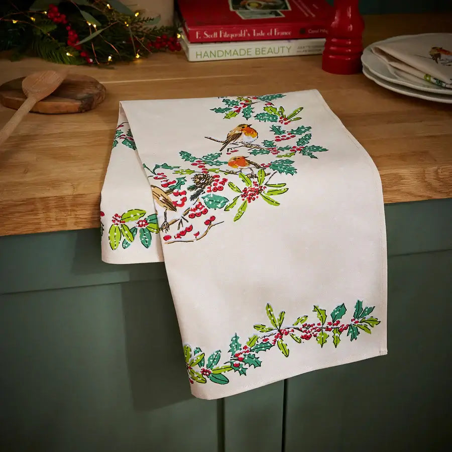 Embroidered table runner with holly design on a wooden table
