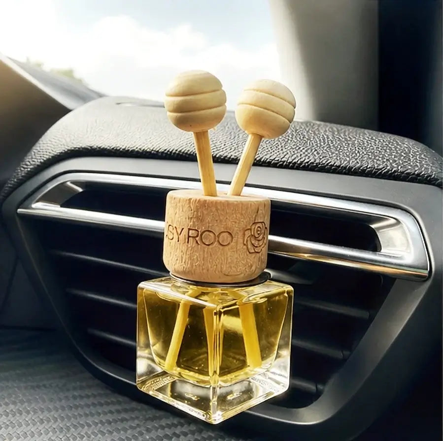 A car air freshener with a clear glass bottle filled with yellow oil and a natural wood cap featuring two round wooden diffuser tops, shown plugged into a car air vent.