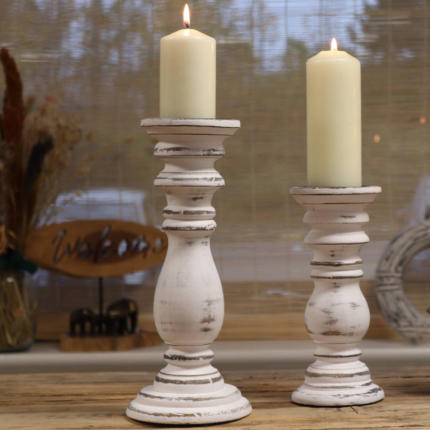 Two white candle holders with candles on a wooden surface.