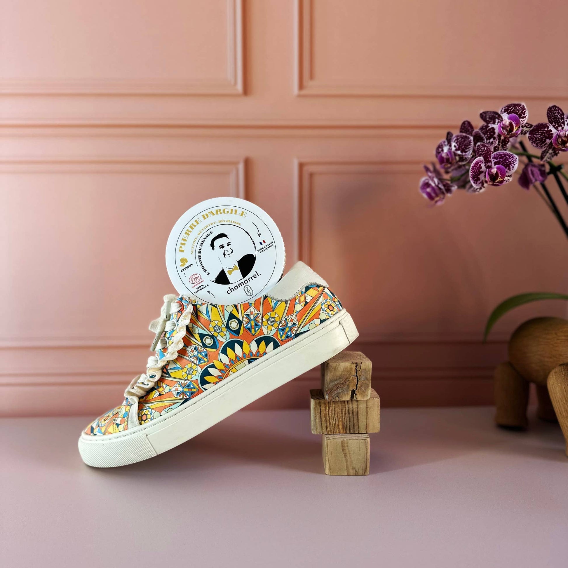 Colorful sneaker with a decorative pattern on a pink surface with a wooden block and plant.