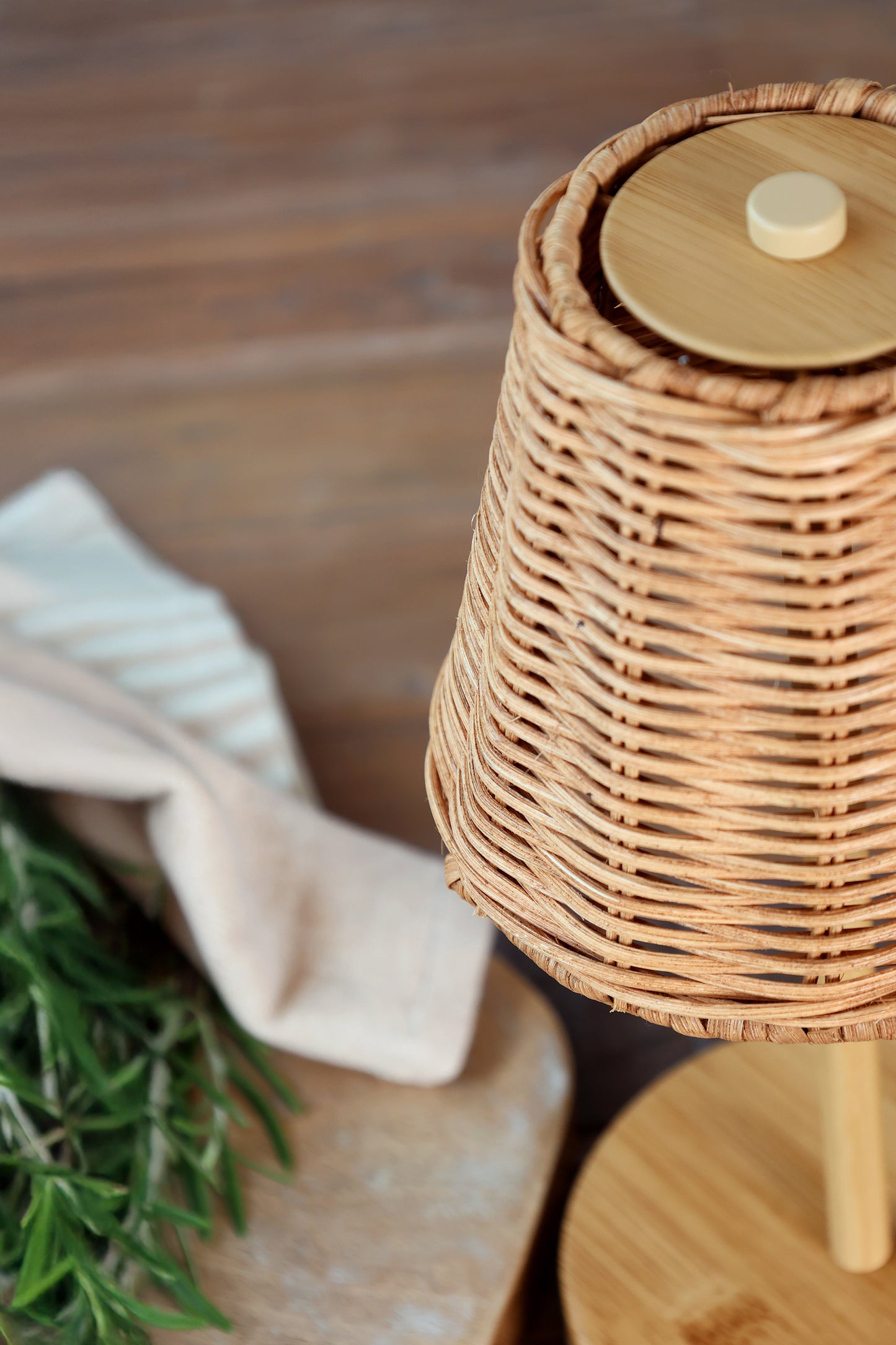 Wicker basket with a wooden lid on a wooden surface with a plant and towel in the background