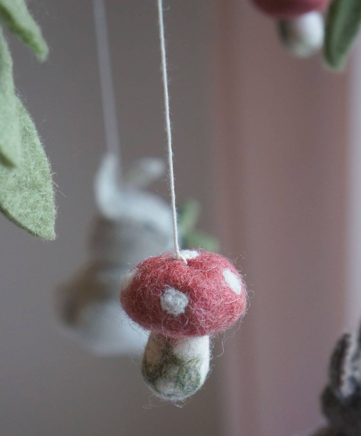Felted mushroom ornament hanging against a blurred background