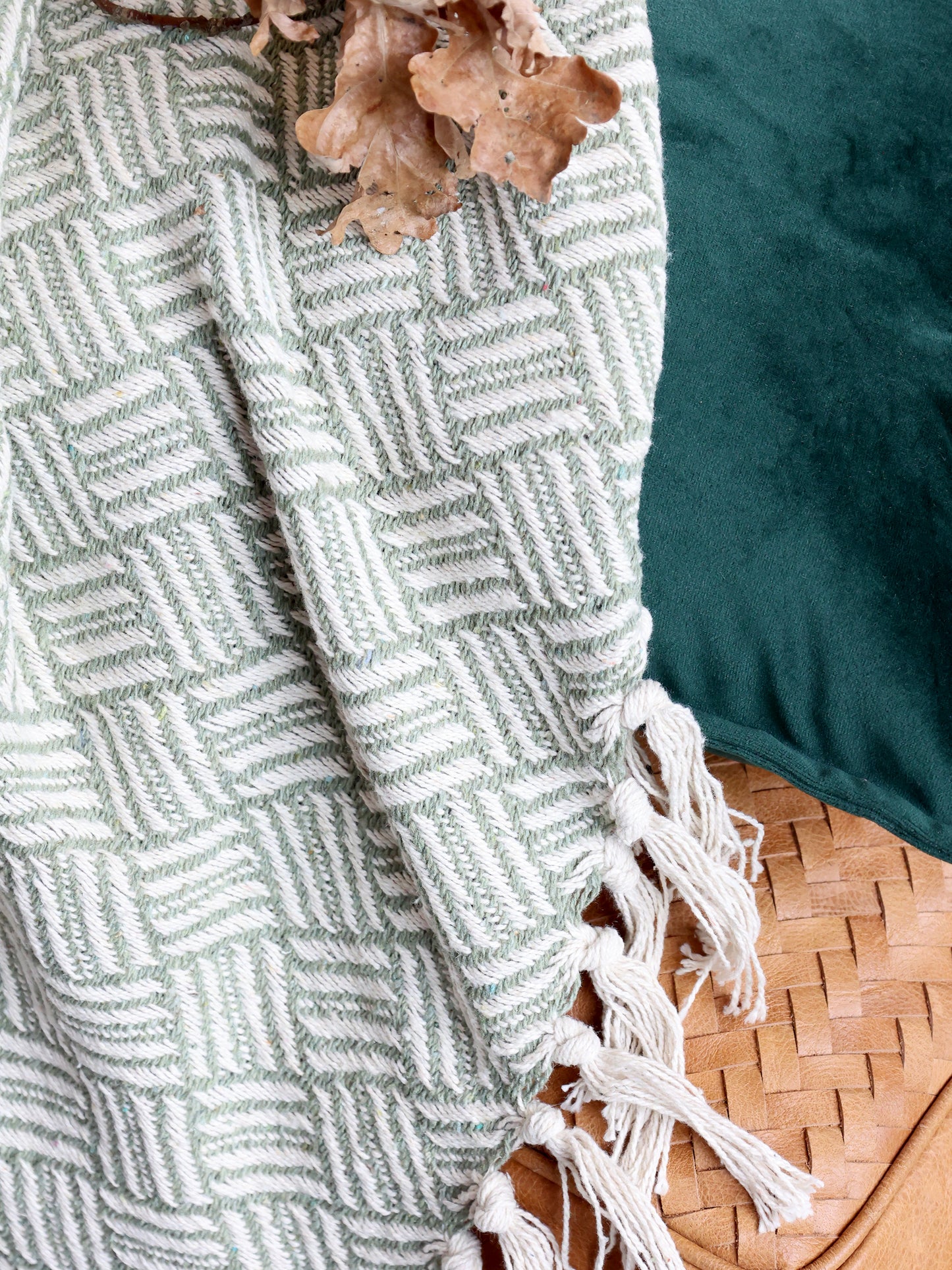 Textured green blanket with white geometric pattern and tassels on a surface.